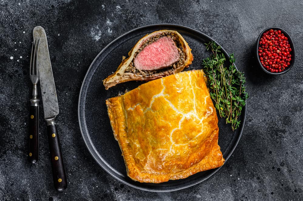 Beef Wellington classic steak dish with tenderloin meat on a plate. Black background. Top view